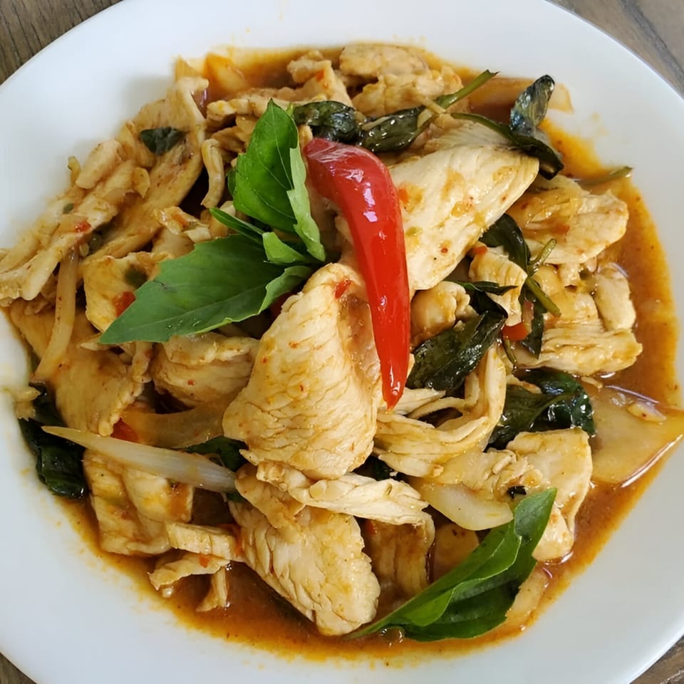 Manow Thai's chicken stir-fry with basil, onions, and a red chili on a white plate.