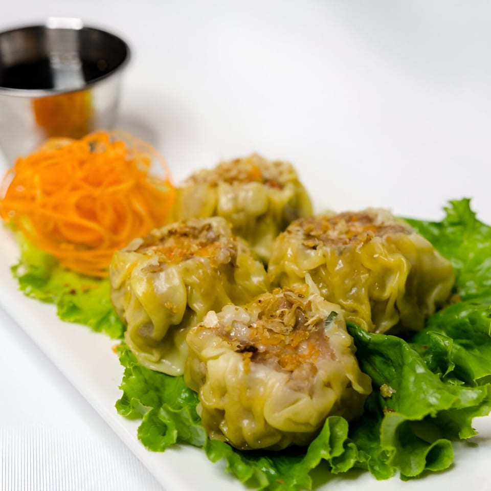 Four steamed dumplings on lettuce with shredded carrots and a dipping sauce cup.