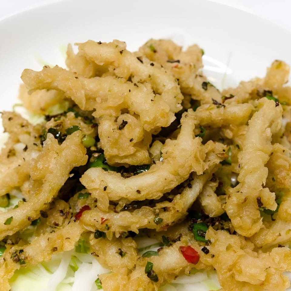 Crispy fried calamari with green herbs and red chili flakes on a bed of shredded cabbage.