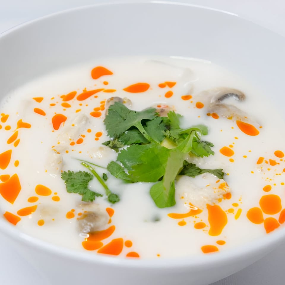 Close-up of Manow Thai's Tom Kha Gai soup with chicken, mushrooms, cilantro, and chili oil.