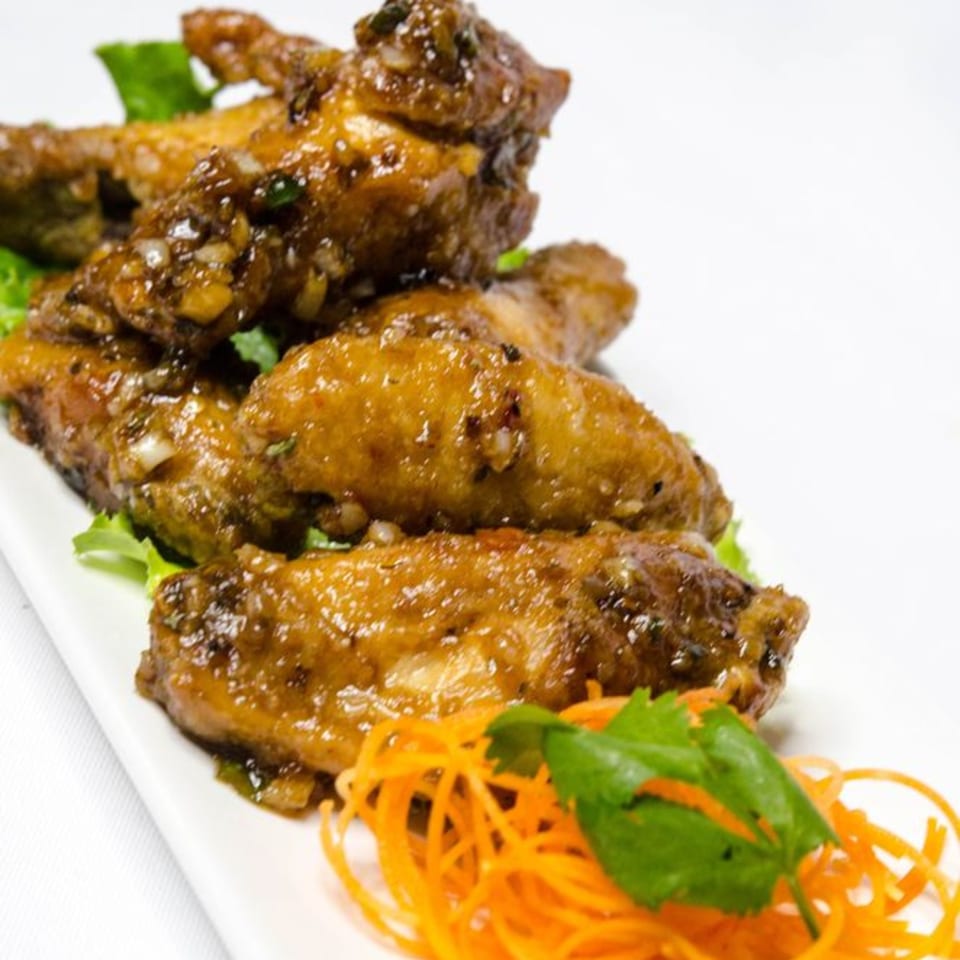 Manow Thai's crispy garlic chicken wings, garnished with shredded carrots and cilantro on a white plate.